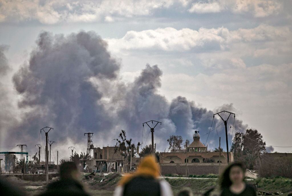 Personas observan el humo que dejan las bombas en Baghuz en Siria