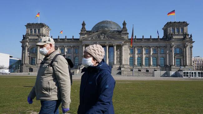 BERLIN, GERMANY - MARCH 25: An elderly couple wearing protective masks and who said they did not mind being photographed walk past the Reichstag where inside the Bundestag is likely later today to pass a massive federal financial aid package to shore Germany up against the effects of the coronavirus on March 25, 2020 in Berlin, Germany. The Bundestag is expected to pass the package worth over EUR 150 billion later today. (Photo by Sean Gallup/Getty Images)