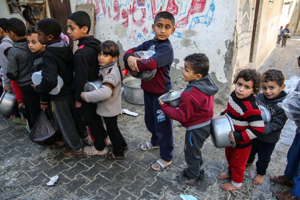 Niños palestinos hacen fila con recipientes para recibir algo de comida en Gaza