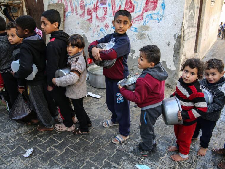 Niños palestinos hacen fila con recipientes para recibir algo de comida en Gaza