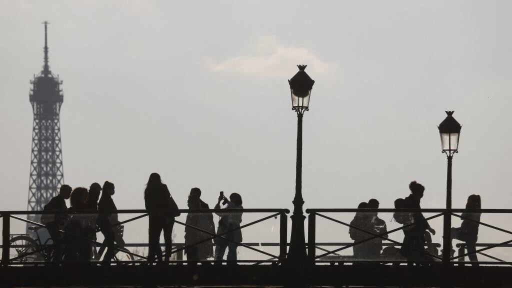 People walk on the Pont des Arts over the river Seine, with the Eiffel Tower in the background, before the curfew, aimed to curb the spread of the Covid-19, in Paris on April 19, 2021. (Photo by Ludovic MARIN / AFP) (Photo by LUDOVIC MARIN/AFP via Getty Images)