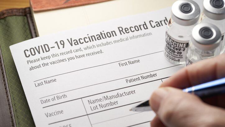 Covid-19 vaccination record card with vials and syringe. Pfizer, Moderna, Johnson & Johnson