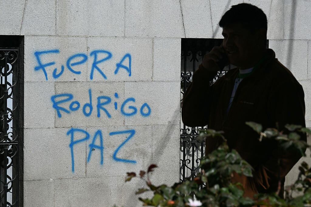 A man walks past a graffiti reading "Rodrigo Paz out," referring to Bolivia's President in La Paz, on May 19, 2026, the day after a protest in demand of his resignation. Bolivian protests calling for center-right President Rodrigo Paz to resign intensified on May 18, 2026 as demonstrators swarmed government buildings and a protest leader faced terrorism charges over the unrest. Riot police clashed with protesters for hours, tear gas shrouded the streets of La Paz, shops were shuttered and supplies ran low due to protest blockades choking routes into the capital city. (Photo by AIZAR RALDES / AFP via Getty Images)