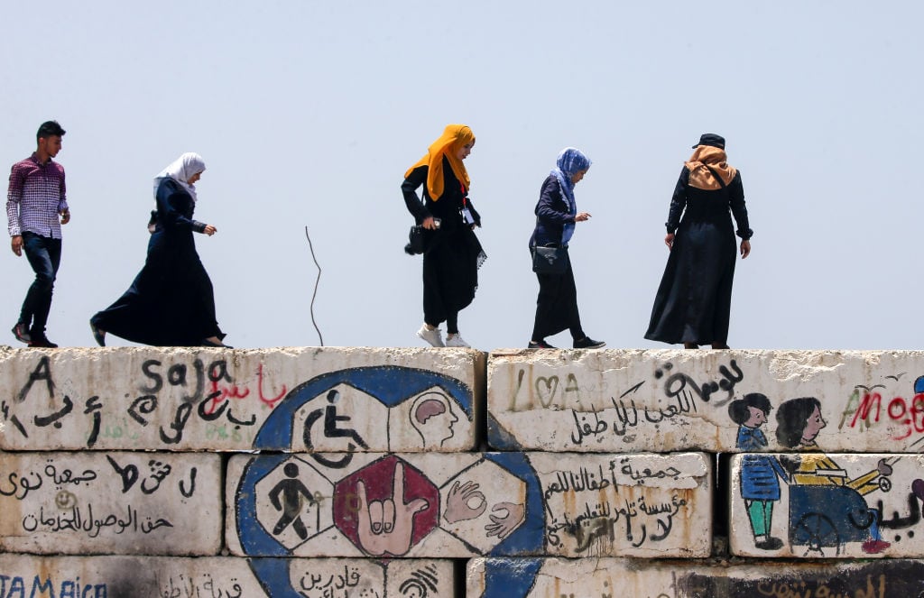 Unas mujeres palestinas caminan sobre un muro en Gaza