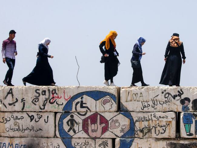 Unas mujeres palestinas caminan sobre un muro en Gaza