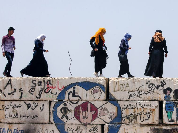 Unas mujeres palestinas caminan sobre un muro en Gaza