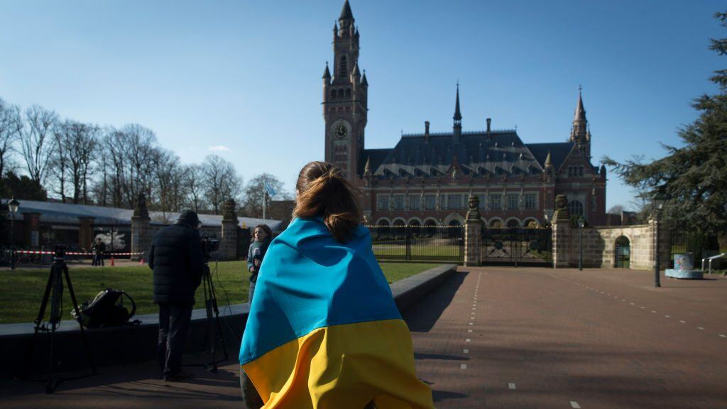 THE HAGUE NETHERLANDS - MARCH 7: A woman with a Ukrainian flag stands outside the International Criminal Court of Justice (ICJ) or Peace Palace on the first day of hearings on March 7, 2022 in The Hague The Netherlands. Ukraine is petitioning the ICJ to classify Russia's invasion as a genocide and issue an injunction under the UN Convention against Genocide. (Photo by Michel Porro/Getty Images)