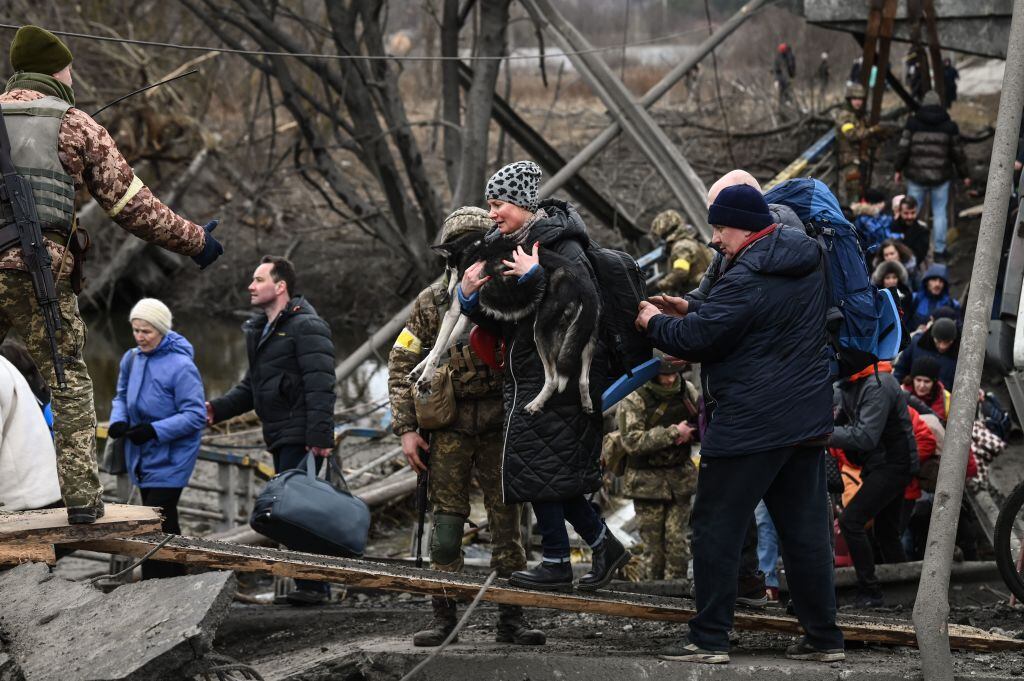 Una mujer lleva un perro mientras la gente cruza un puente destruido mientras evacuan la ciudad de Irpin, al noroeste de Kiev, durante fuertes bombardeos y bombardeos el 5 de marzo de 2022, 10 días después de que Rusia lanzara una invasión militar en Ucrania. (Foto de Aris Messinis / AFP) (Foto de ARIS MESSINIS/AFP vía Getty Images)