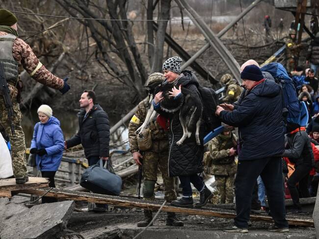 Una mujer lleva un perro mientras la gente cruza un puente destruido mientras evacuan la ciudad de Irpin, al noroeste de Kiev, durante fuertes bombardeos y bombardeos el 5 de marzo de 2022, 10 días después de que Rusia lanzara una invasión militar en Ucrania. (Foto de Aris Messinis / AFP) (Foto de ARIS MESSINIS/AFP vía Getty Images)