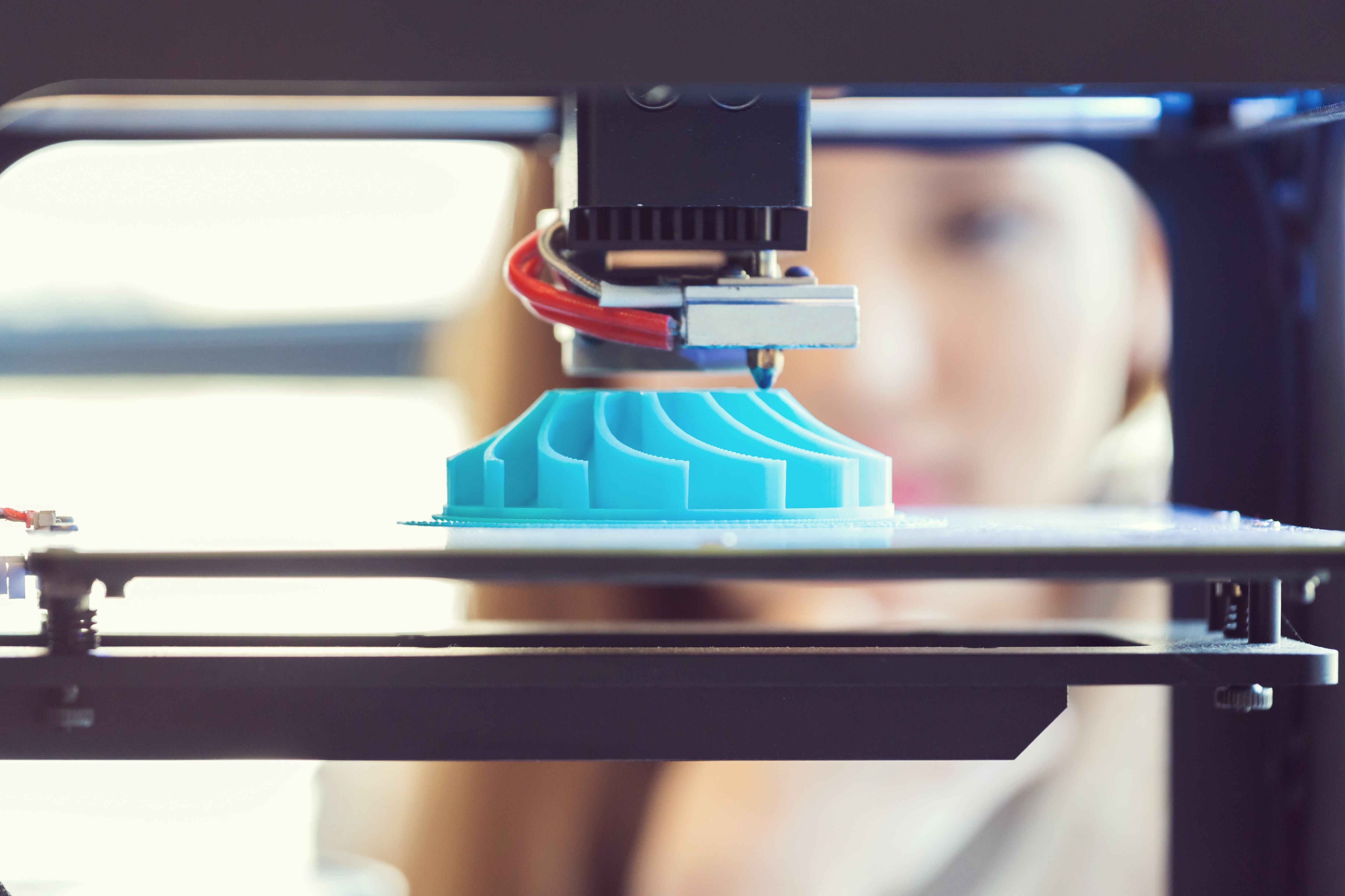 Young woman watching 3D printout. Focus on blue printout.