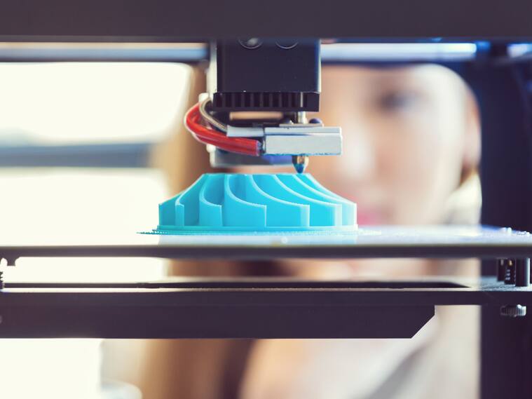 Young woman watching 3D printout. Focus on blue printout.