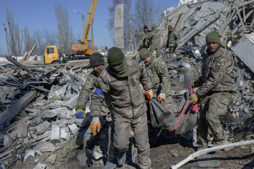 EDITORS NOTE: Graphic content / Ukrainian soldiers carry a dead soldier through debris at the military school hit by Russian rockets the day before, in Mykolaiv, southern Ukraine, on March 19, 2022. - Ukrainian media reported that Russian forces had carried out a large-scale air strike on Mykolaiv, killing at least 40 Ukrainian soldiers at their brigade headquarters. (Photo by BULENT KILIC / AFP) (Photo by BULENT KILIC/AFP via Getty Images)
