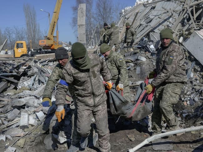 EDITORS NOTE: Graphic content / Ukrainian soldiers carry a dead soldier through debris at the military school hit by Russian rockets the day before, in Mykolaiv, southern Ukraine, on March 19, 2022. - Ukrainian media reported that Russian forces had carried out a large-scale air strike on Mykolaiv, killing at least 40 Ukrainian soldiers at their brigade headquarters. (Photo by BULENT KILIC / AFP) (Photo by BULENT KILIC/AFP via Getty Images)