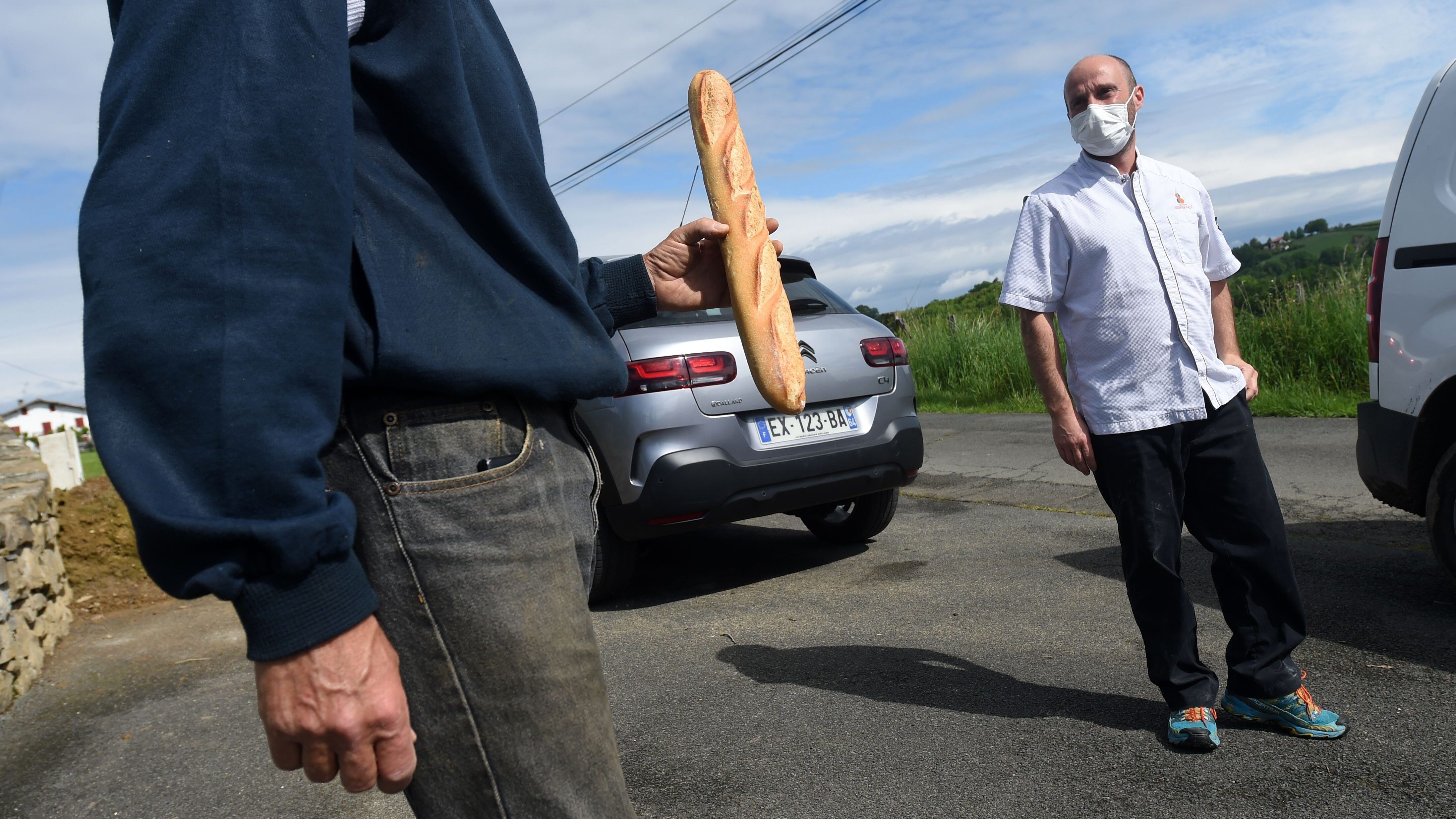 Bruno Berterreix (R), a baker from Espelette, wearing a face mask, delivers bread to a customer in Souraide, southwestern France, on April 28, 2020, on the 43rd day of a lockdown in France aimed at curbing the spread of the COVID-19 disease, caused by the novel coronavirus. (Photo by GAIZKA IROZ / AFP) (Photo by GAIZKA IROZ/AFP via Getty Images)