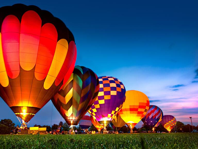 Muggy, hot, humid summer night lit by the glow of a row of hot air balloons. This was ballooning festival was located in Monore, Wisconsin. The glowing fiery heat of the burners creates a surreal glow.