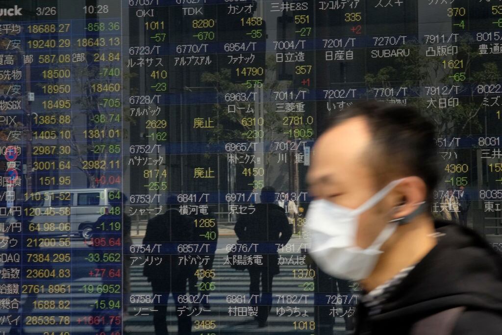 Pedestrians walk in front of a quotation board displaying stock prices on the Tokyo Stock Exchange in Tokyo on March 26, 2020. - Tokyo's key Nikkei index opened down more than three percent on March 26 on profit-taking after surging in recent sessions, although US stimulus plans offset worries over the COVID-19 coronavirus pandemic. (Photo by Kazuhiro NOGI / AFP) (Photo by KAZUHIRO NOGI/AFP via Getty Images)