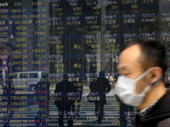 Pedestrians walk in front of a quotation board displaying stock prices on the Tokyo Stock Exchange in Tokyo on March 26, 2020. - Tokyo's key Nikkei index opened down more than three percent on March 26 on profit-taking after surging in recent sessions, although US stimulus plans offset worries over the COVID-19 coronavirus pandemic. (Photo by Kazuhiro NOGI / AFP) (Photo by KAZUHIRO NOGI/AFP via Getty Images)