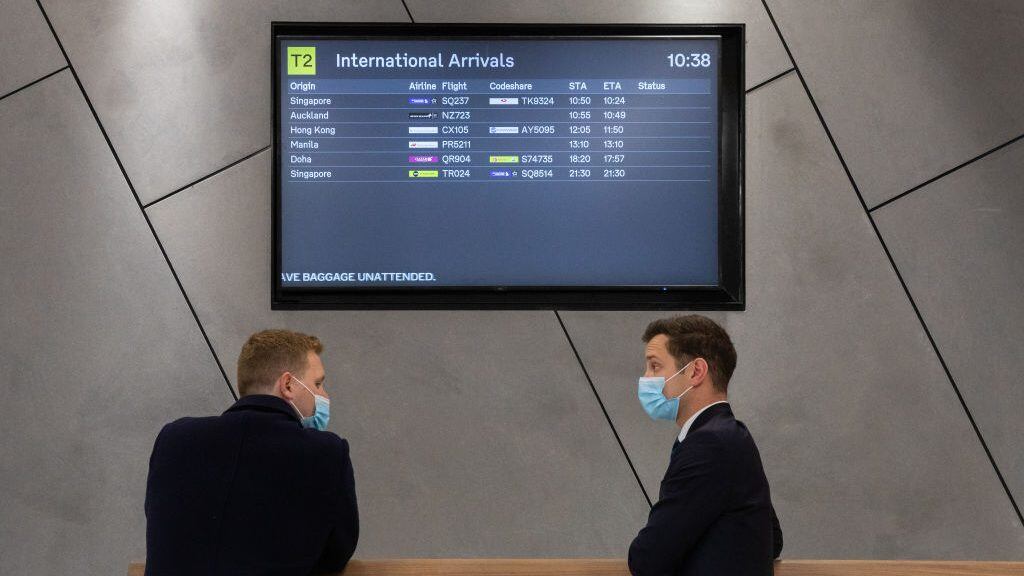 MELBOURNE, AUSTRALIA - DECEMBER 07: Two men wearing masks standing in front of a International arrivals board at the international arrivals terminal at Melbourne Airport on December 07, 2020 in Melbourne, Australia. International flights have resumed into Melbourne as Victoria's COVID-19 coronavirus restrictions continue to ease. Mask-wearing is now only mandatory in indoor shopping centres and public transport, including rideshares and taxis, but relaxed in other settings. Victorians must still carry a mask with them at all times and wear it when a physical distance of 1.5 metres cannot be maintained, but mask use is encouraged, but not mandatory, in other situations. Cafes, restaurants and pubs can double their patron numbers to a maximum of one person per 2 sq m and nightclubs can reopen from midnight. People are able to have up to 30 visitors at home, while outdoor gatherings can now have up to 100 people. (Photo by Asanka Ratnayake/Getty Images)