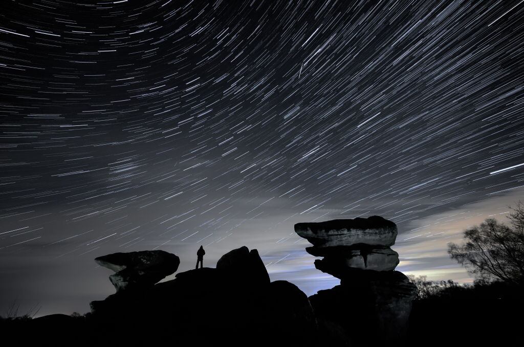 EDITORS NOTE EFFECT CREATED BY OVERLAYING MULTIPLE FRAMES SHOT CONSECUTIVELY FROM A SINGLE CAMERA A man watches a meteor during the Geminid meteor shower over Brimham Rocks, a collection of balancing rock formations in the Nidderdale Area of Outstanding Natural Beauty in North Yorkshire. (Photo by Danny Lawson/PA Images via Getty Images)