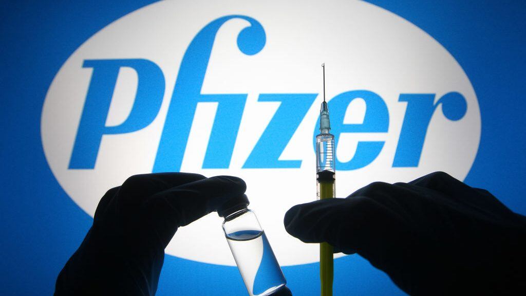 UKRAINE - 2021/04/27: In this photo illustration, silhouette of hands in medical gloves hold a medical syringe and a vial in front of Pfizer logo of an US pharmaceutical industry company. (Photo Illustration by Pavlo Gonchar/SOPA Images/LightRocket via Getty Images)