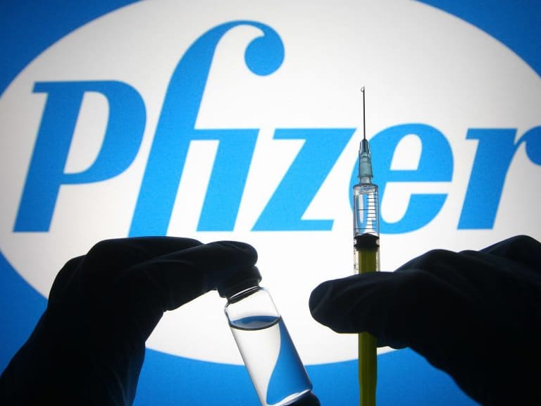 UKRAINE - 2021/04/27: In this photo illustration, silhouette of hands in medical gloves hold a medical syringe and a vial in front of Pfizer logo of an US pharmaceutical industry company. (Photo Illustration by Pavlo Gonchar/SOPA Images/LightRocket via Getty Images)