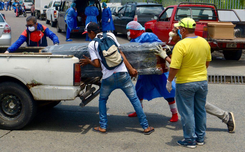 02 April 2020, Ecuador, Guayaquil: Men with protective suits load a coffin into a car in front of the hospital General del Guasmo. The port city of Guayaquil is the most affected by Covid-19 in Ecuador. Dead bodies lie in the apartments for days, the morgues of the hospitals are overcrowded. The city administration requested four refrigerated containers in which the corpses can be temporarily stored. Photo: Marcos Pin Mendez/dpa (Photo by Marcos Pin Mendez/picture alliance via Getty Images)