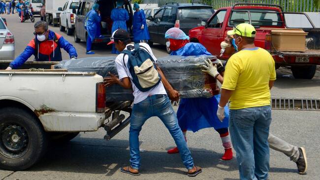 02 April 2020, Ecuador, Guayaquil: Men with protective suits load a coffin into a car in front of the hospital General del Guasmo. The port city of Guayaquil is the most affected by Covid-19 in Ecuador. Dead bodies lie in the apartments for days, the morgues of the hospitals are overcrowded. The city administration requested four refrigerated containers in which the corpses can be temporarily stored. Photo: Marcos Pin Mendez/dpa (Photo by Marcos Pin Mendez/picture alliance via Getty Images)
