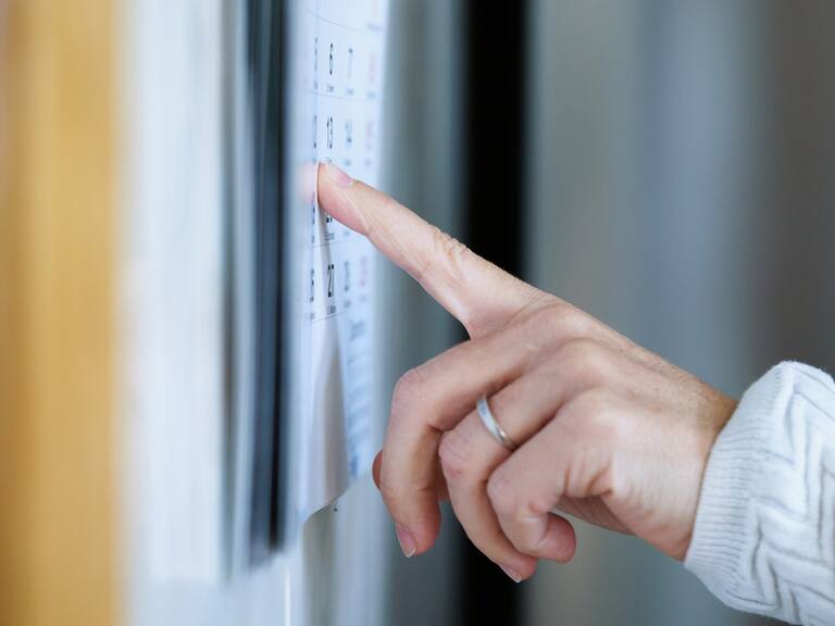 A woman's hand with a wedding ring points with her finger to a date on a cardboard calendar. A woman points to a calendar's day