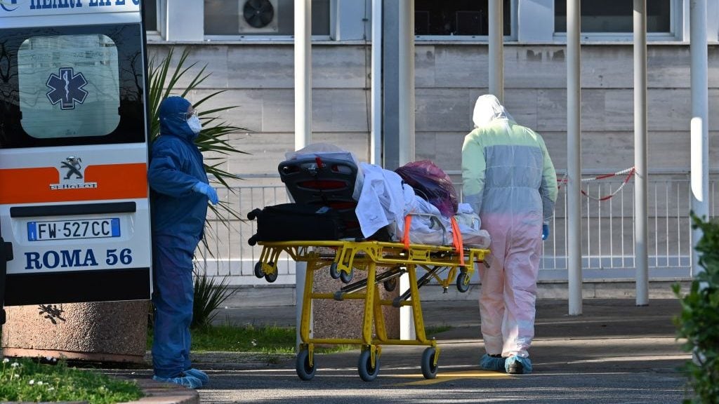 Male nurses wearing a face mask and overalls bring a patient on a stretcher into the newly built Columbus Covid 2 temporary hospital to fight the new coronavirus infection, on March 16, 2020 at the Gemelli hospital in Rome. (Photo by ANDREAS SOLARO / AFP) (Photo by ANDREAS SOLARO/AFP via Getty Images)