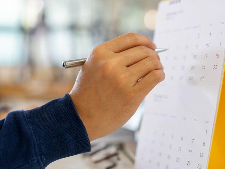 close up on employee man hand using finger pointing schedule (timetable) on calendar to writing list of job and make appointment meeting or manage timetable each day , life balance concept
