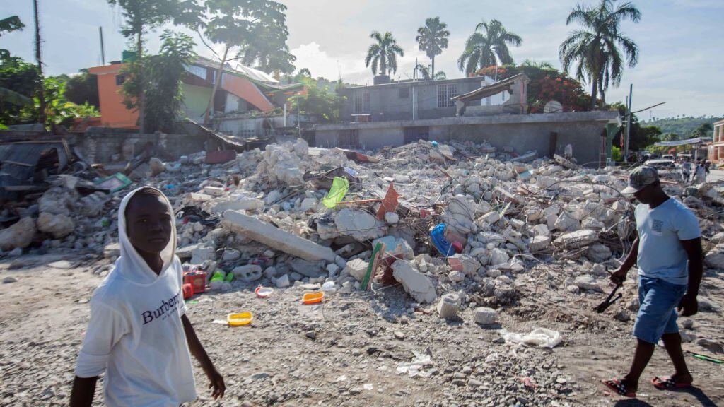 LES CAYES, HAITI - AUGUST 16: Men walk among the debris of a collapsed building after a 7.2-magnitude earthquake struck Haiti on August 16, 2021 in Corvalion, Les Cayes, Haiti. Rescue workers have been working among destroyed homes since the quake struck on Saturday and so far there are 1,297 dead and 5.700 wounded. The epicenter was located about 100 miles west of the capital city Port-au-Prince. (Photo by Richard Pierrin/Getty Images)