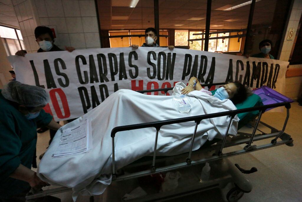 SANTIAGO, CHILE - JUNE 16: A COVID-19 patient passes in front of nurses who hold a billboard that read in Spanish "Tents are for camping not for hospitals" during a visit by newly appointed Health Minister Enrique Paris on June 16, 2020 in Santiago, Chile. On Monday, President Piñera extended the State of Catastrophe for 90 days to better control the outbreak of COVID-19 in the country. (Photo by Marcelo Hernandez/Getty Images)