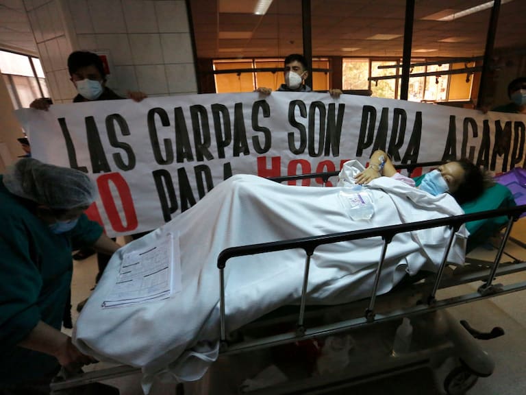 SANTIAGO, CHILE - JUNE 16: A COVID-19 patient passes in front of nurses who hold a billboard that read in Spanish &quot;Tents are for camping not for hospitals&quot; during a visit by newly appointed Health Minister Enrique Paris on June 16, 2020 in Santiago, Chile. On Monday, President Piñera extended the State of Catastrophe for 90 days to better control the outbreak of COVID-19 in the country. (Photo by Marcelo Hernandez/Getty Images)