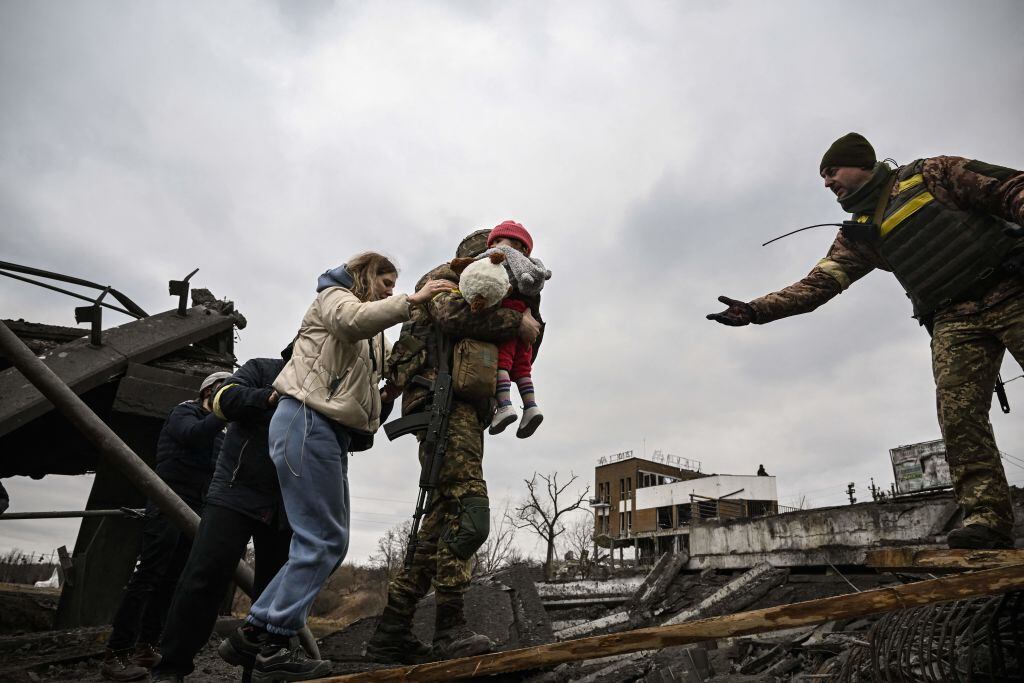TOPSHOT – Un militar ucraniano carga a un niño mientras ayuda a las personas a cruzar un puente destruido mientras evacuan la ciudad de Irpin, al noroeste de Kiev, durante fuertes bombardeos y bombardeos el 5 de marzo de 2022, 10 días después de que Rusia lanzara una invasión militar en Ucrania. . (Foto de Aris Messinis / AFP) (Foto de ARIS MESSINIS/AFP vía Getty Images)
