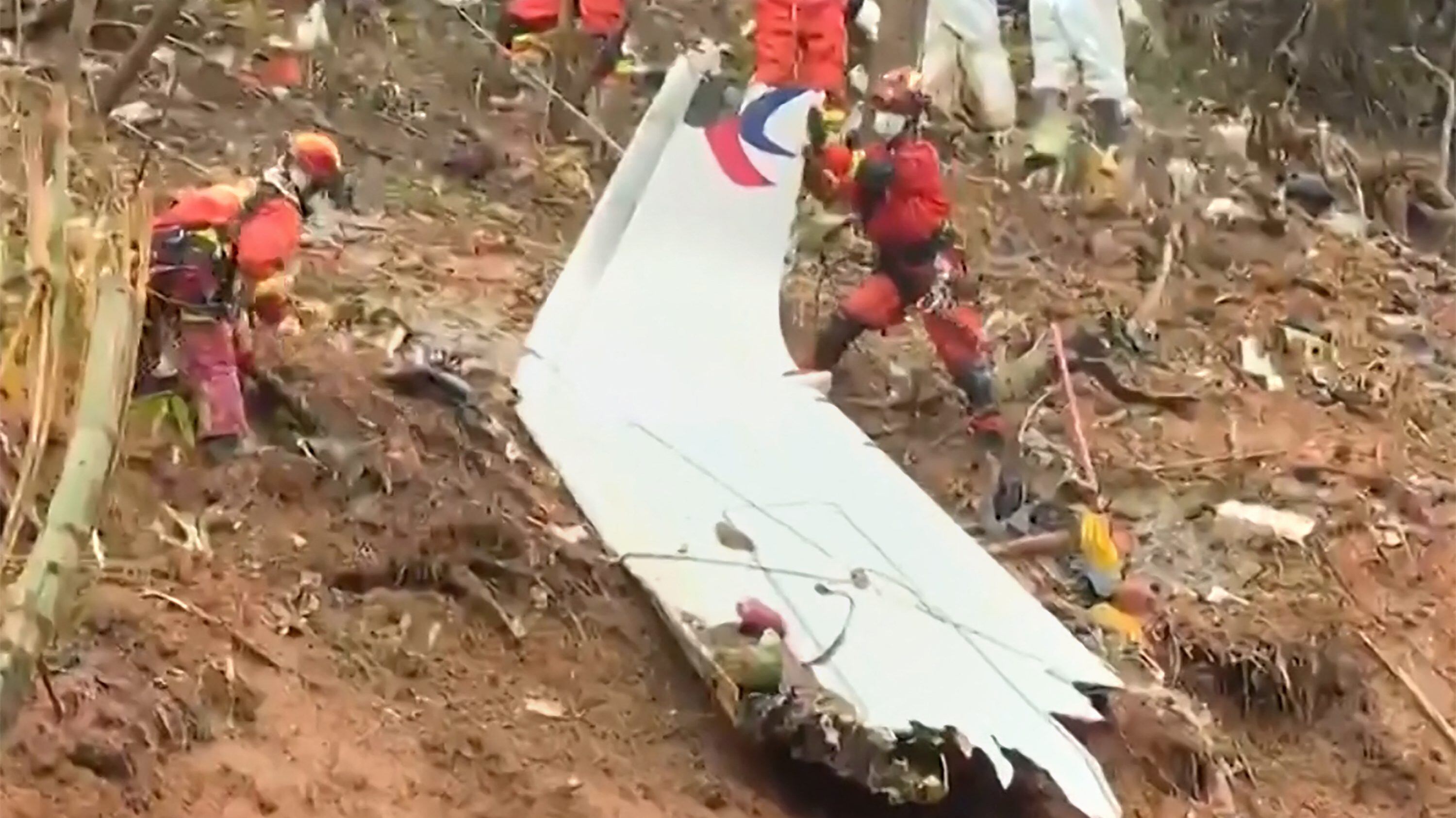 This screengrab taken on March 24, 2022 from video by state broadcaster China Central Television (CCTV) via AFPTV shows rescue teams with a piece of the fuselage as they continue their search at the site of where a China Eastern passenger jet crashed onto a mountainside near Wuzhou City in China's southern Guangxi region. - The cause of the disaster which killed 132 people has mystified aviation authorities who have scoured rugged terrain for clues, finding no survivors from what is almost certain to be China's deadliest plane crash in nearly 30 years. - China OUT (Photo by various sources / AFP) / China OUT (Photo by STR/AFPTV/AFP via Getty Images)