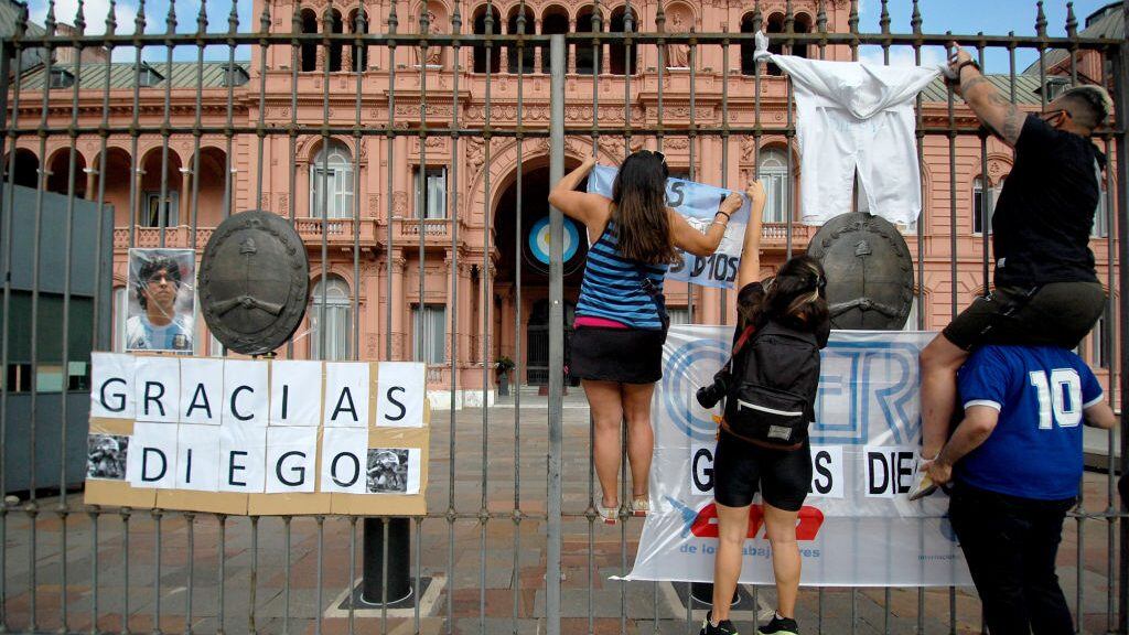 BUENOS AIRES, ARGENTINA - NOVEMBER 25, 2020: People hang posters outside the Casa Rosada presidential residence after the news on the death of Argentina's football legend Diego Maradona. One of the best football players the 20th century, Maradona won the 1986 World Cup with Argentina's national team; he played for the Argentine clubs Argentinos Juniors, Boca Juniors, and Newell's Old Boys, Spain's FC Barcelona and Sevilla FC, and Italy's Napoli. Maradona won Italy's Serie A and Coppa Italia, Spain's Copa del Rey and Copa de la Liga, and the UEFA Cup; he played in 687 matches scoring the total of 363 goals, including 113 matches and 50 goals for the national team of Argentina. Yelena Kondratyeva/TASS (Photo by Yelena KondratyevaTASS via Getty Images)