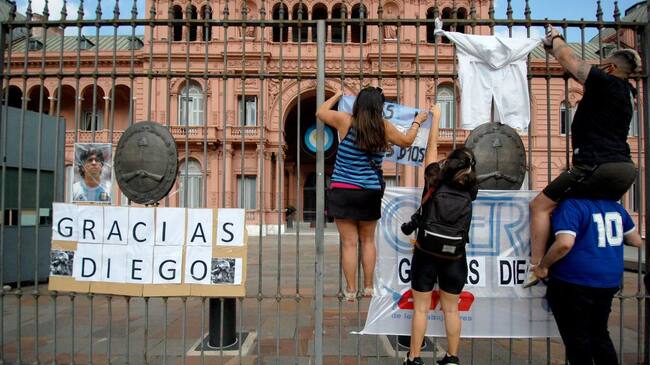 BUENOS AIRES, ARGENTINA - NOVEMBER 25, 2020: People hang posters outside the Casa Rosada presidential residence after the news on the death of Argentina's football legend Diego Maradona. One of the best football players the 20th century, Maradona won the 1986 World Cup with Argentina's national team; he played for the Argentine clubs Argentinos Juniors, Boca Juniors, and Newell's Old Boys, Spain's FC Barcelona and Sevilla FC, and Italy's Napoli. Maradona won Italy's Serie A and Coppa Italia, Spain's Copa del Rey and Copa de la Liga, and the UEFA Cup; he played in 687 matches scoring the total of 363 goals, including 113 matches and 50 goals for the national team of Argentina. Yelena Kondratyeva/TASS (Photo by Yelena KondratyevaTASS via Getty Images)