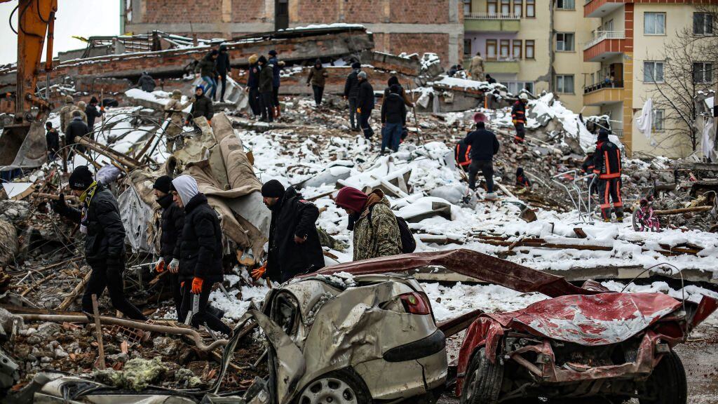 MALATYA, TURKIYE- FEBRUARY 7: People walk by as rescue workers search amongst the rubble after the earthquake struck on February 7, 2023 in Malatya, Türkiye. An earthquake with a magnitude of 7.8 occurred in the Pazarcık district of Kahramanmaraş ruins on February 6.  (Photo by Hakan Akgun/ dia images)