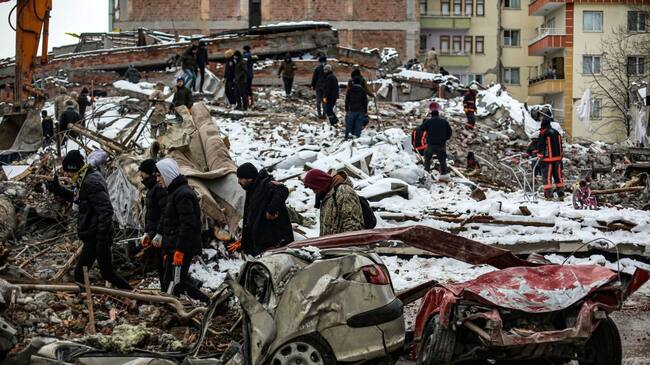 MALATYA, TURKIYE- FEBRUARY 7: People walk by as rescue workers search amongst the rubble after the earthquake struck on February 7, 2023 in Malatya, Türkiye. An earthquake with a magnitude of 7.8 occurred in the Pazarcık district of Kahramanmaraş ruins on February 6. (Photo by Hakan Akgun/ dia images)