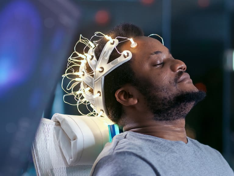 In Laboratory Man Wearing Brainwave Scanning Headset Sits in a Chair with Closed Eyes. Monitors Show EEG Reading and Graphical Brain Model. In the Modern Brain Study/ Neurological Research Laboratory.