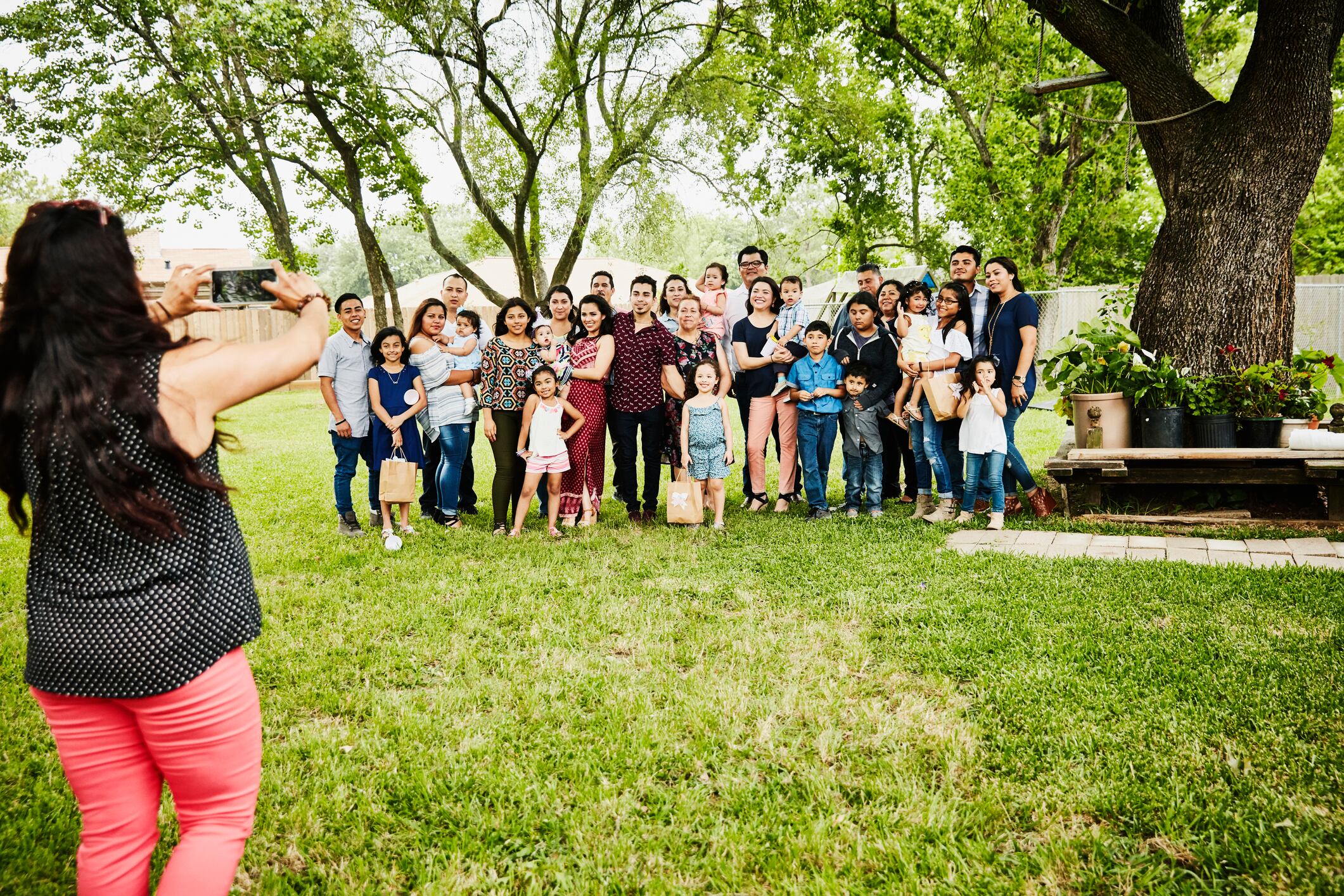 Woman taking photo of smiling multigenerational family gather for backyard birthday party