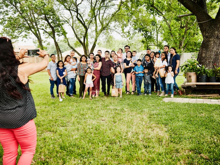 Woman taking photo of smiling multigenerational family gather for backyard birthday party