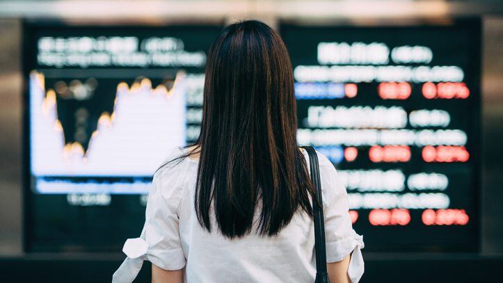Rear view of businesswoman looking at stock exchange market display screen board in downtown financial district