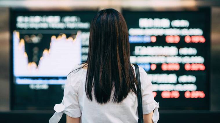 Rear view of businesswoman looking at stock exchange market display screen board in downtown financial district