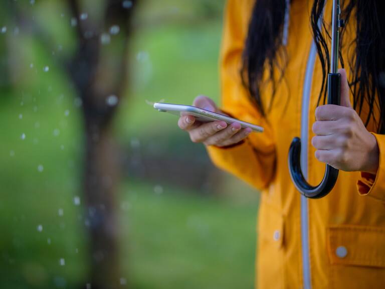 Midsection shot of a woman in a yellow raincoat using her phone