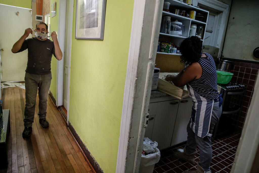 Marcela Hueichapan (R) prepares dough to make bread while Ramon Canales puts on a face mask in Santiago, on April 28, 2020. - Without the possibility of working due to restrictions imposed during the Covid-19 pandemic, many Chileans had to reinvent themselves to subsist taking advantage of what was closest at their fingertips, such as making bread in their homes and selling them among their neighbors. (Photo by JAVIER TORRES / AFP) (Photo by JAVIER TORRES/AFP via Getty Images)