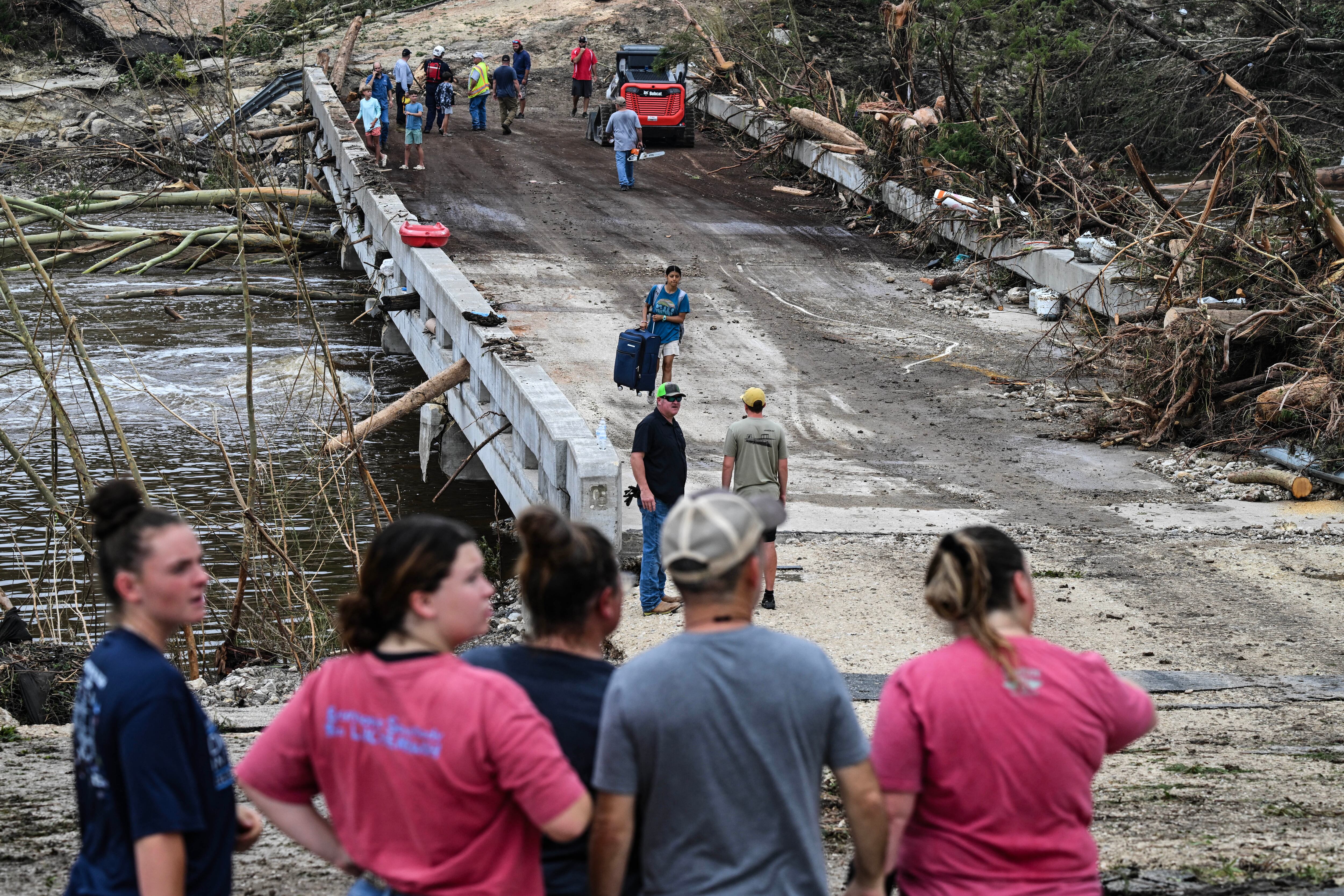 TOPSHOT - People look on as law enforcement and volunteers continue to search for missing people near Camp Mystic, the site of where at least 20 girls went missing after flash flooding in Hunt, Texas, on July 5, 2025. Rescuers were on Saturday searching for more than 20 girls missing from a riverside summer camp in the US state of Texas, after torrential rains caused devastating flooding that killed at least 27 people -- with more rain on the way. "So far, we've evacuated over 850 uninjured people, eight injured people and have recovered 27 deceased fatalities at this time. Of these 27, 18 are adults, nine are children," said Kerr Country Sheriff Larry Leitha on July 5. (Photo by RONALDO SCHEMIDT / AFP) (Photo by RONALDO SCHEMIDT/AFP via Getty Images)          