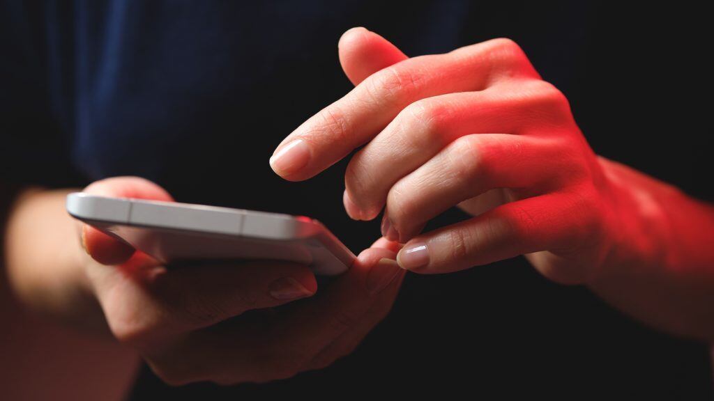 Mobile phone in the hands of a girl. A young woman in a black t-shirt is holding a phone. An email fraudster sends a message. The work of a freelancer, businessman.