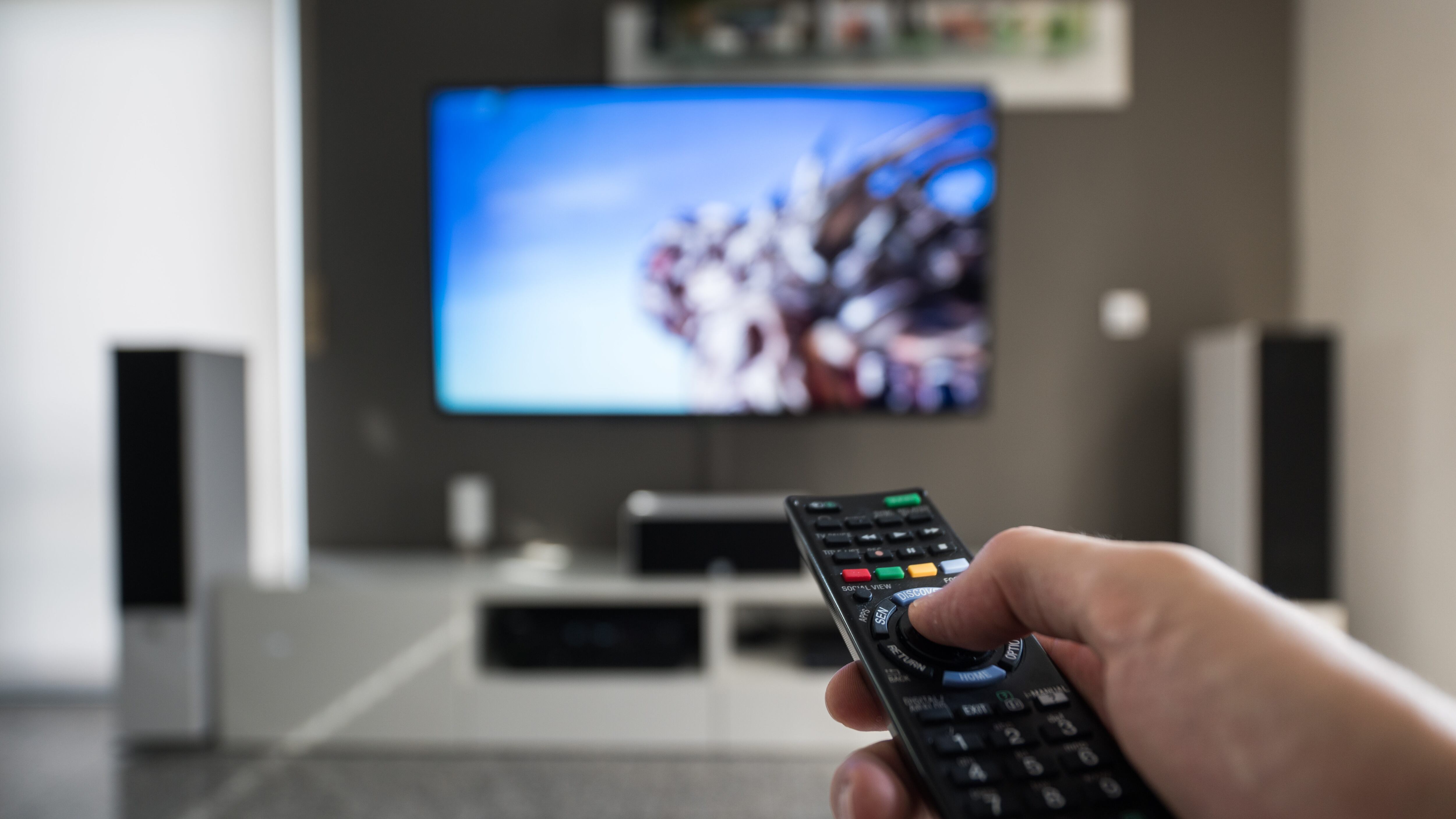 A man is switching through television channels. Captured inside a modern living room at daytime.