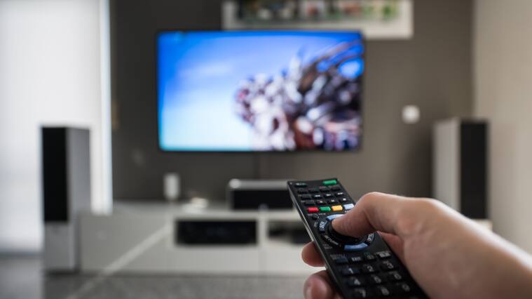 A man is switching through television channels. Captured inside a modern living room at daytime.